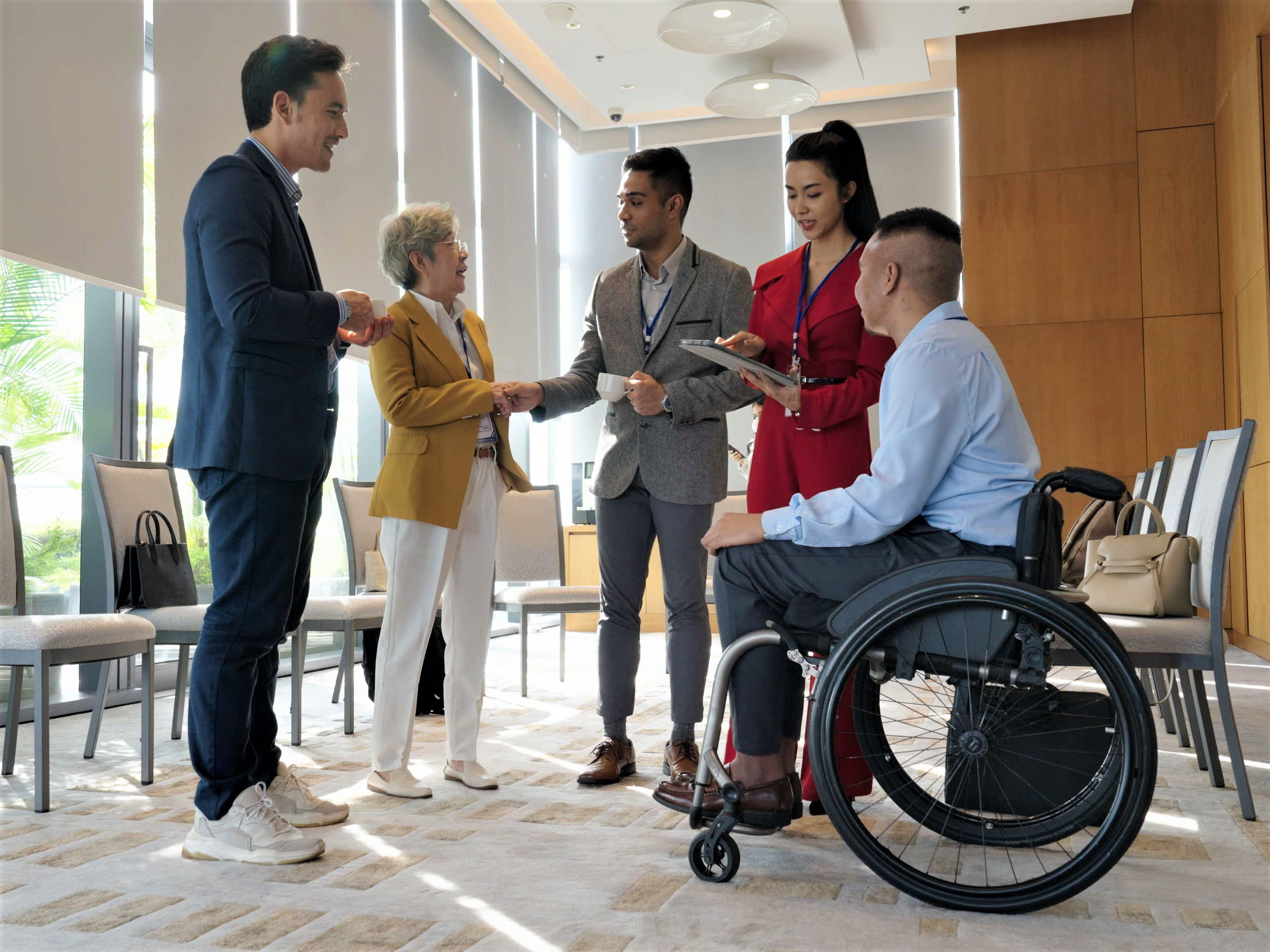 Diverse professionals, including a wheelchair user, networking and shaking hands in a meeting room.